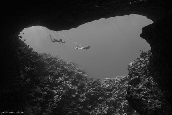 underwater photography of two people swimming outside cave