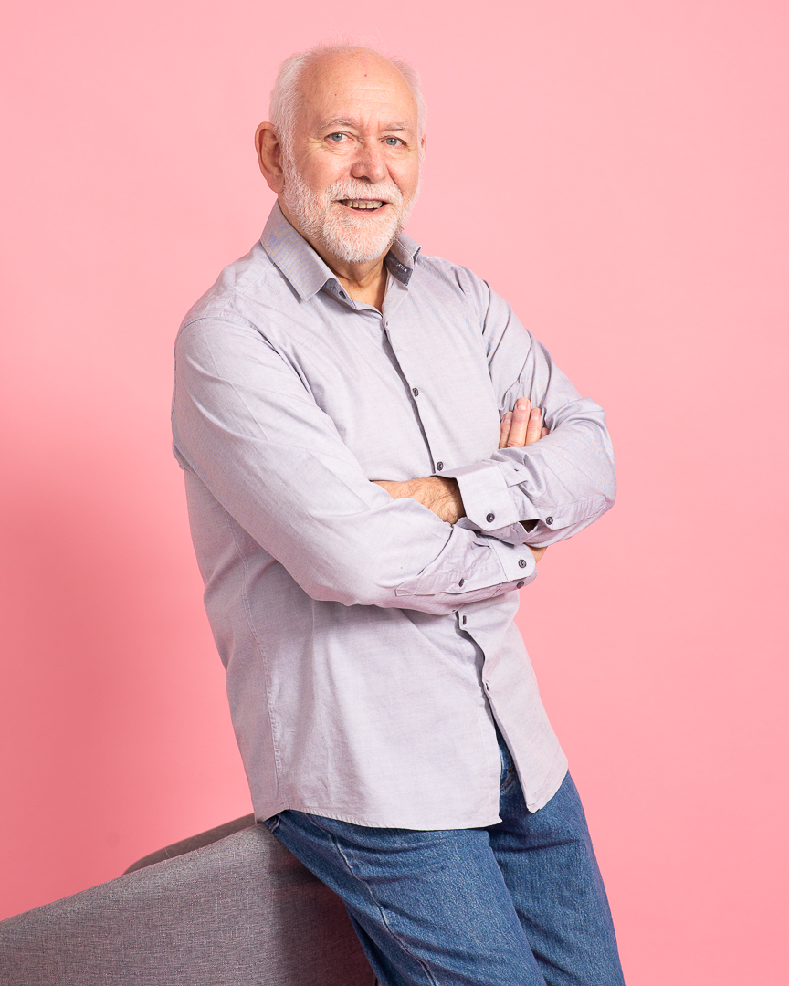 Melbourne man smiles to camera with arms crossed on a pink studio background