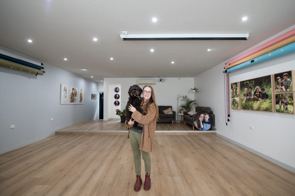 Julia Nance standing in her melbourne portrait studio holding her dog Felix.
