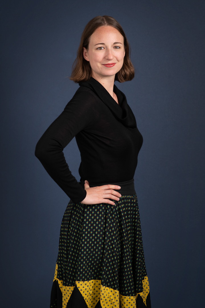 Professional corporate headshot of woman smiling softly to camera on a navy blue background.