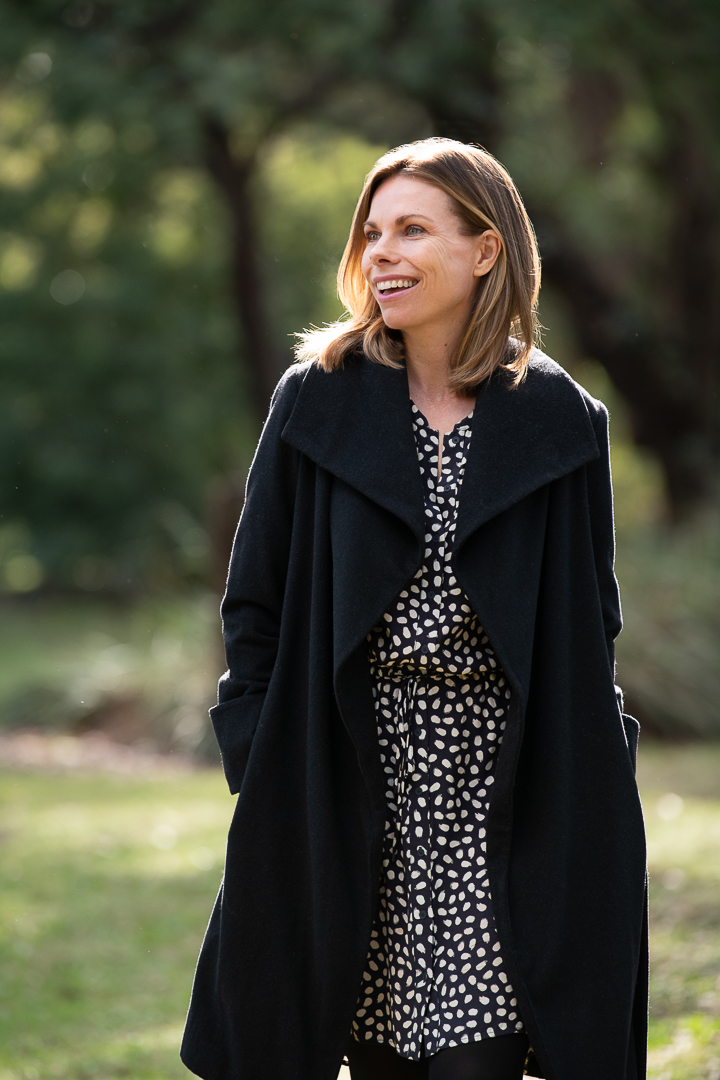 Personal branding author portrait of woman in winter coat, smiling and looking away from the camera in an outdoor setting.