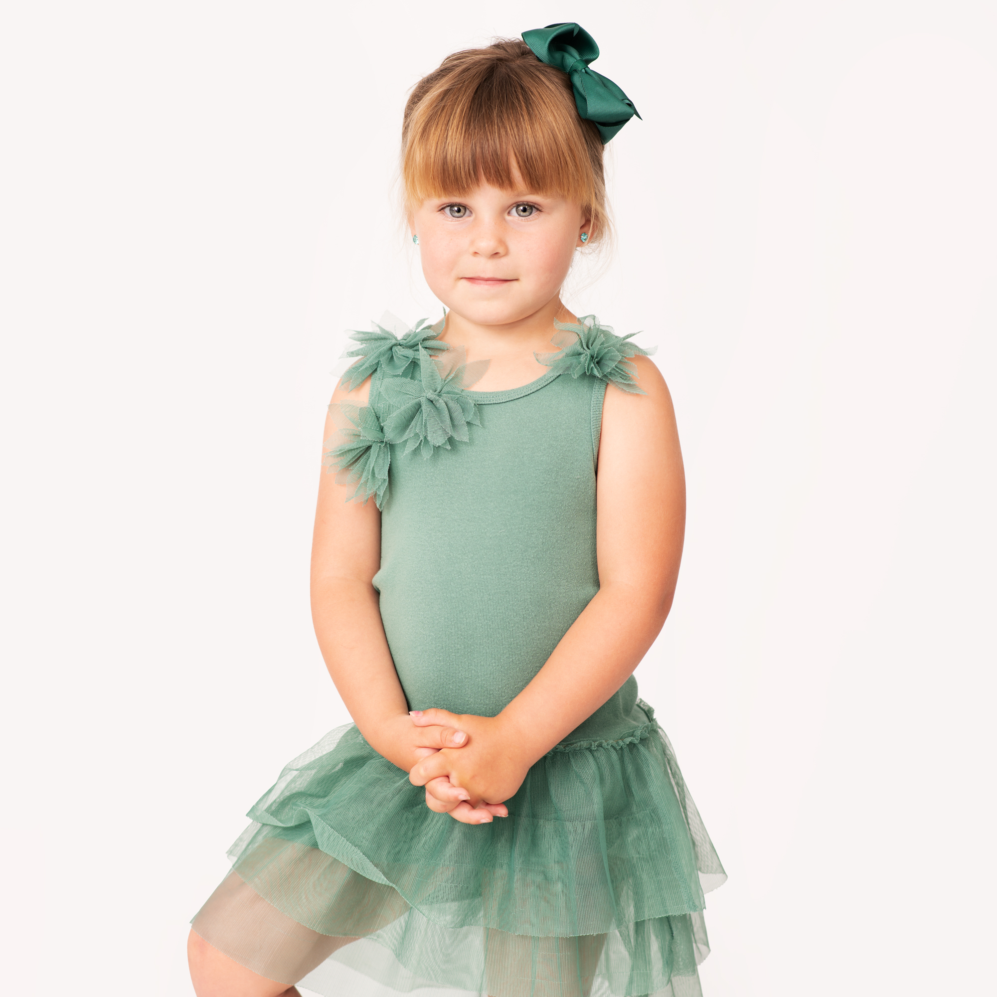A young girl poses for her childrens model portfolio session. She wears a green dress on a white background.