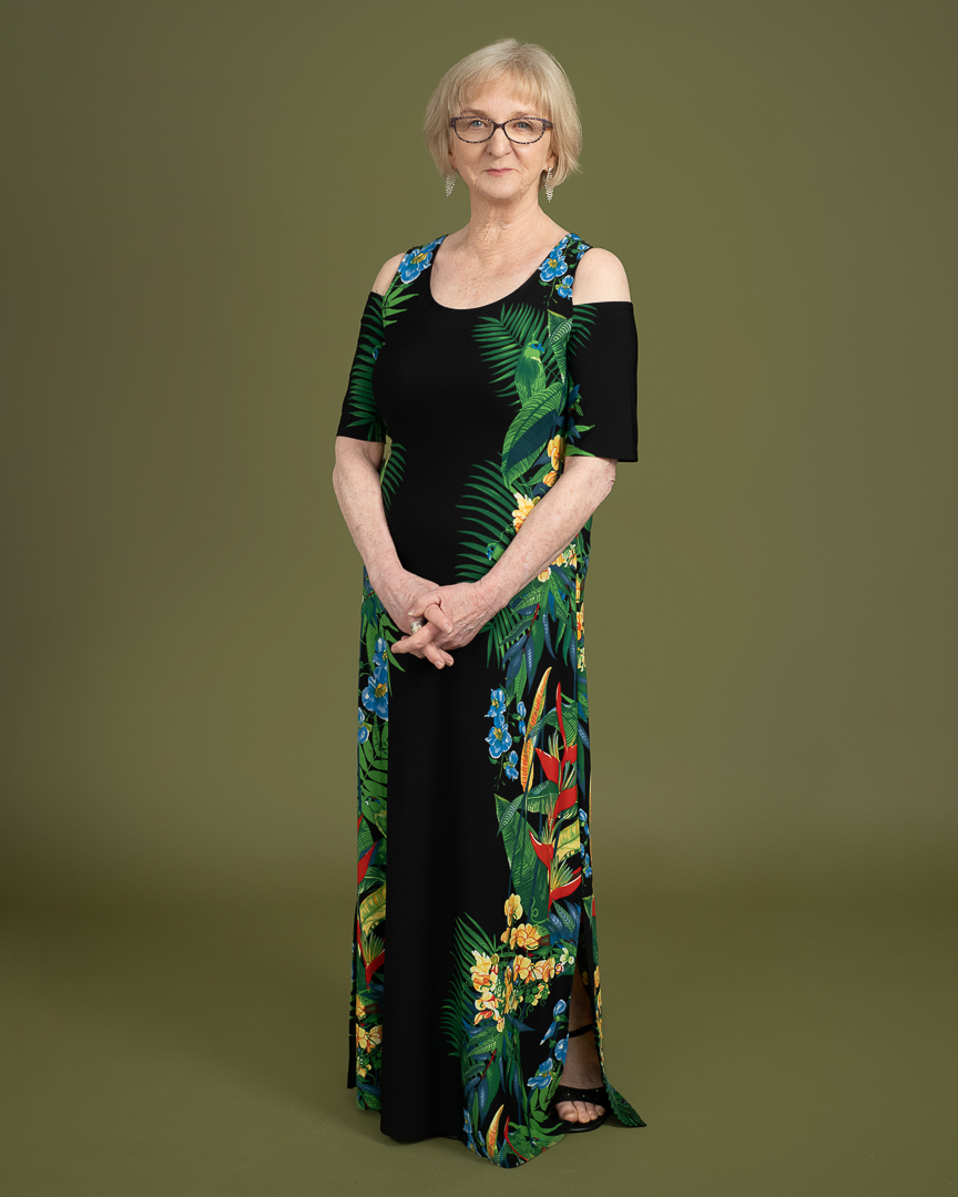 Melbourne actress stands for full length portrait in studio on a green background. She wears a long floor length dress and smiles to camera.