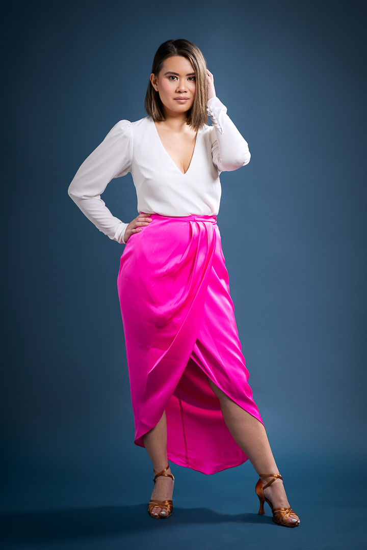Melbourne small business owner stands confidently in her personal branding photoshoot. She is photographed in studio wearing a hot pink skirt and white top, on a navy background.
