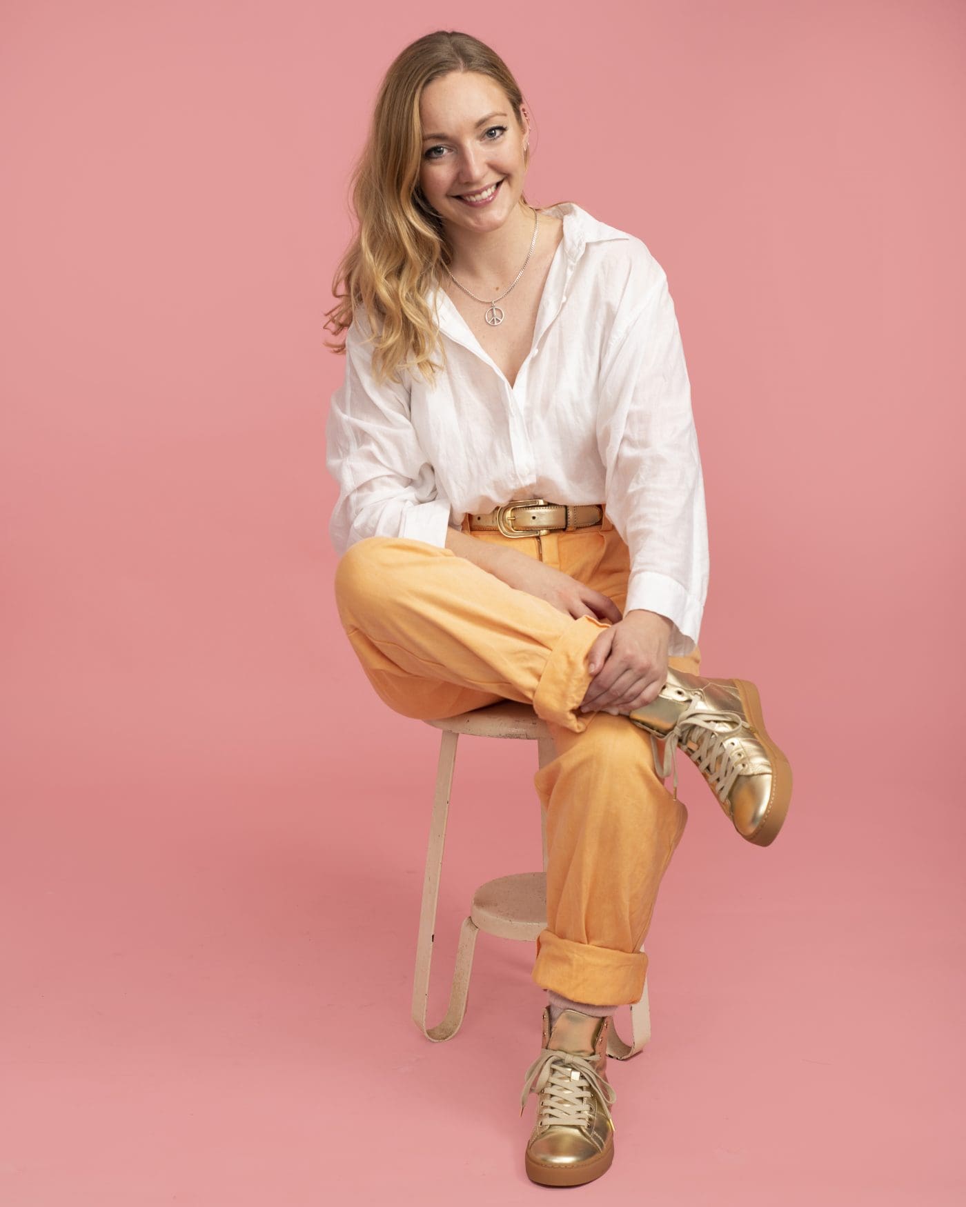 Melbourne business owner sits in a relaxed poses wearing a white shirt and yellow pants. She smiles to camera for a personal branding portrait.