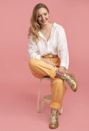 Melbourne business owner sits in a relaxed poses wearing a white shirt and yellow pants. She smiles to camera for a personal branding portrait.