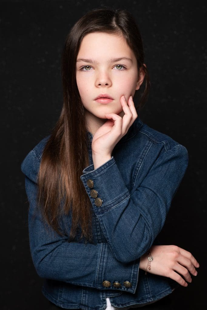 A studio portrait of young Melbourne actress and dancer who wears a denim jacket and looks to camera with one hand on her cheek.