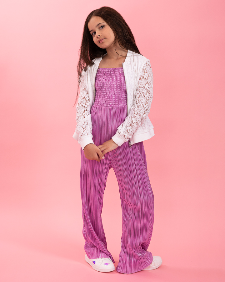 Teen girl poses in purple jumpsuit on a pink studio background for her model portfolio photoshoot.