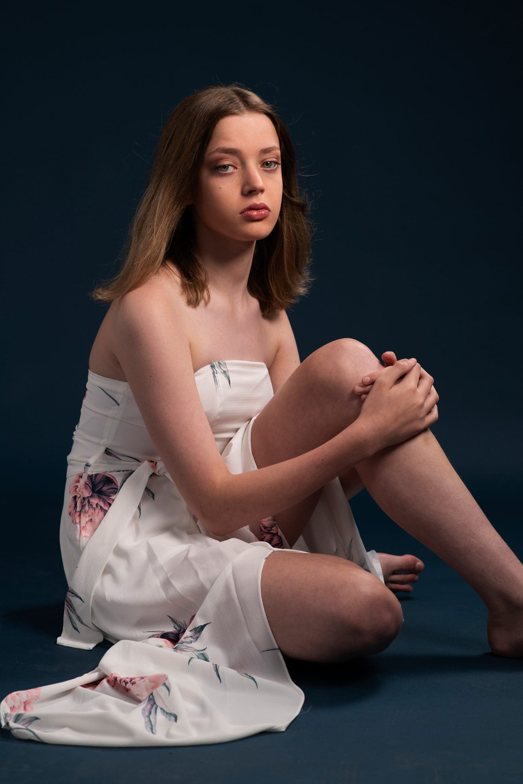 Melbourne teen model portfolio update taken in studio on a navy background. model wears a white floral dress and has a relaxed pose.