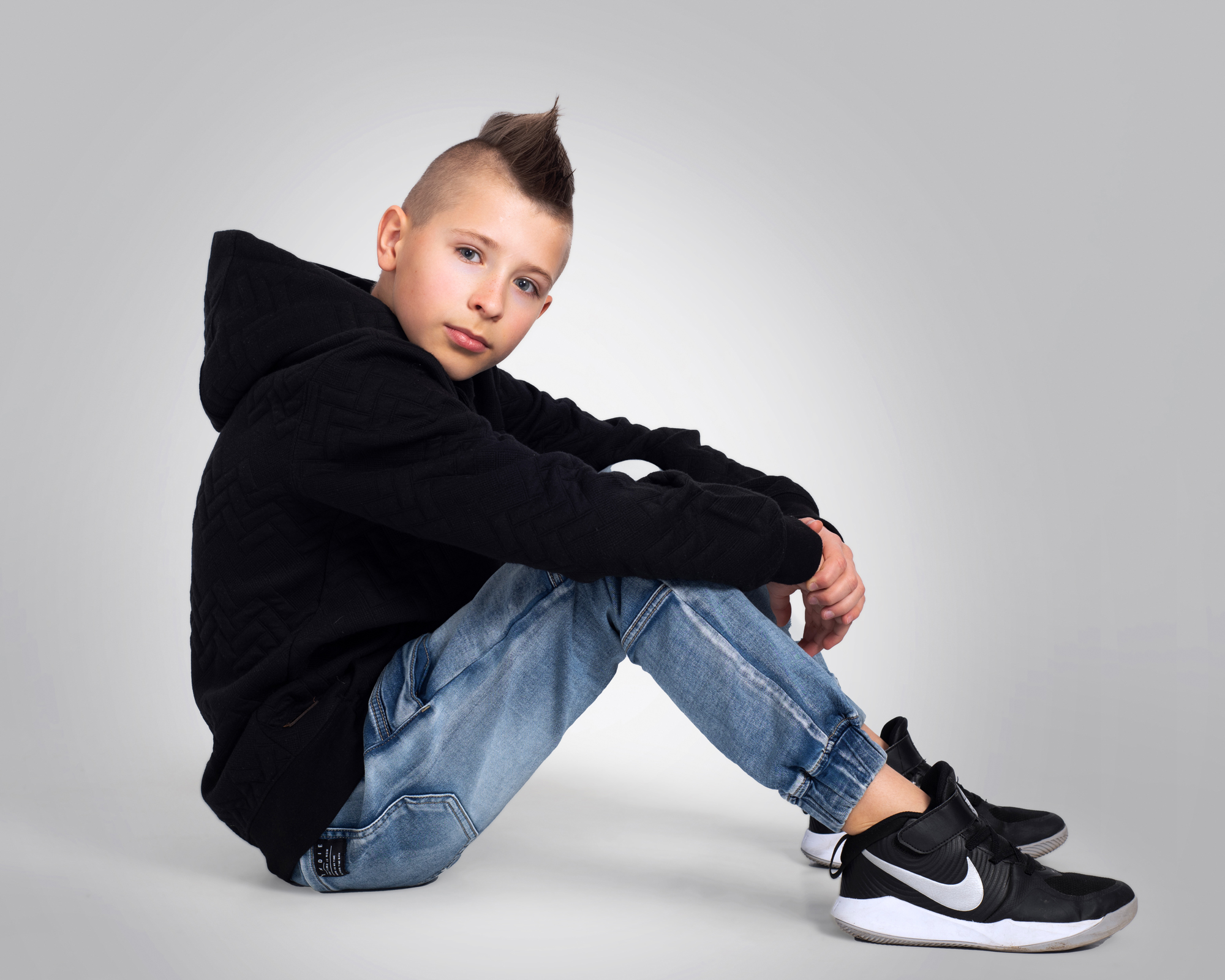 teen model sits in studio looking to camera for a model portfolio session, wearing streetwear.