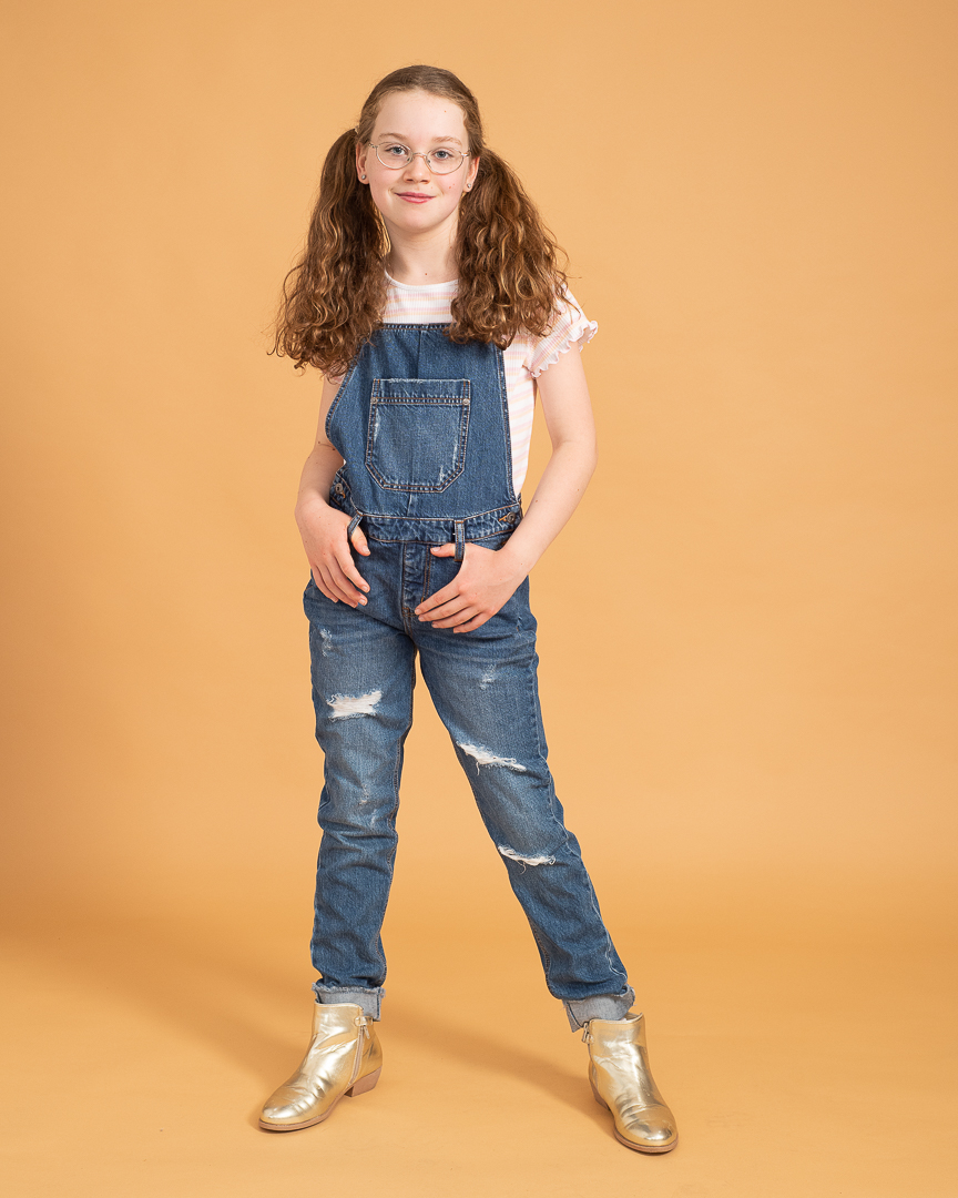Young melbourne actor and dancer poses in a full length portrait for a portfolio update. She wears denim overalls, pigtails and glasses and smiles at the camera with a confident pose.