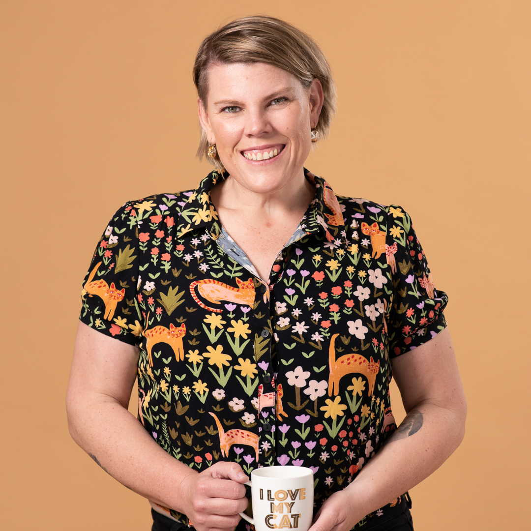Woman stands in studio holding a cup of coffee and smiles to camera in a relaxed and natural personal branding portrait.