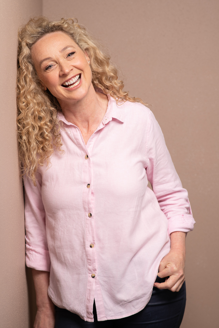 A relaxed and natural branding portrait of Melbourne actress Angela, who wears a pink collared shirt and laughs to camera.
