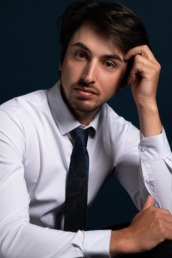 Close up model headshot of male model looking to camera while wearing a white shirt and tie.