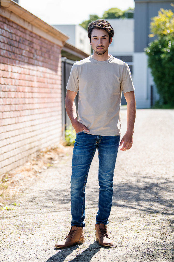 Melbourne model portrait of male model in an urban setting. He wears a casual tshirt and blue jeans, with one hand in his pocket and a serious expression.