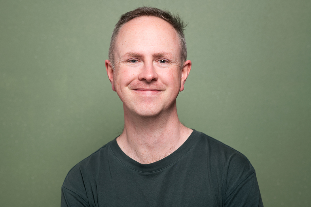A happy and relaxed studio headshot of melbourne man wearing a green tshirt on a green background, taken in studio.