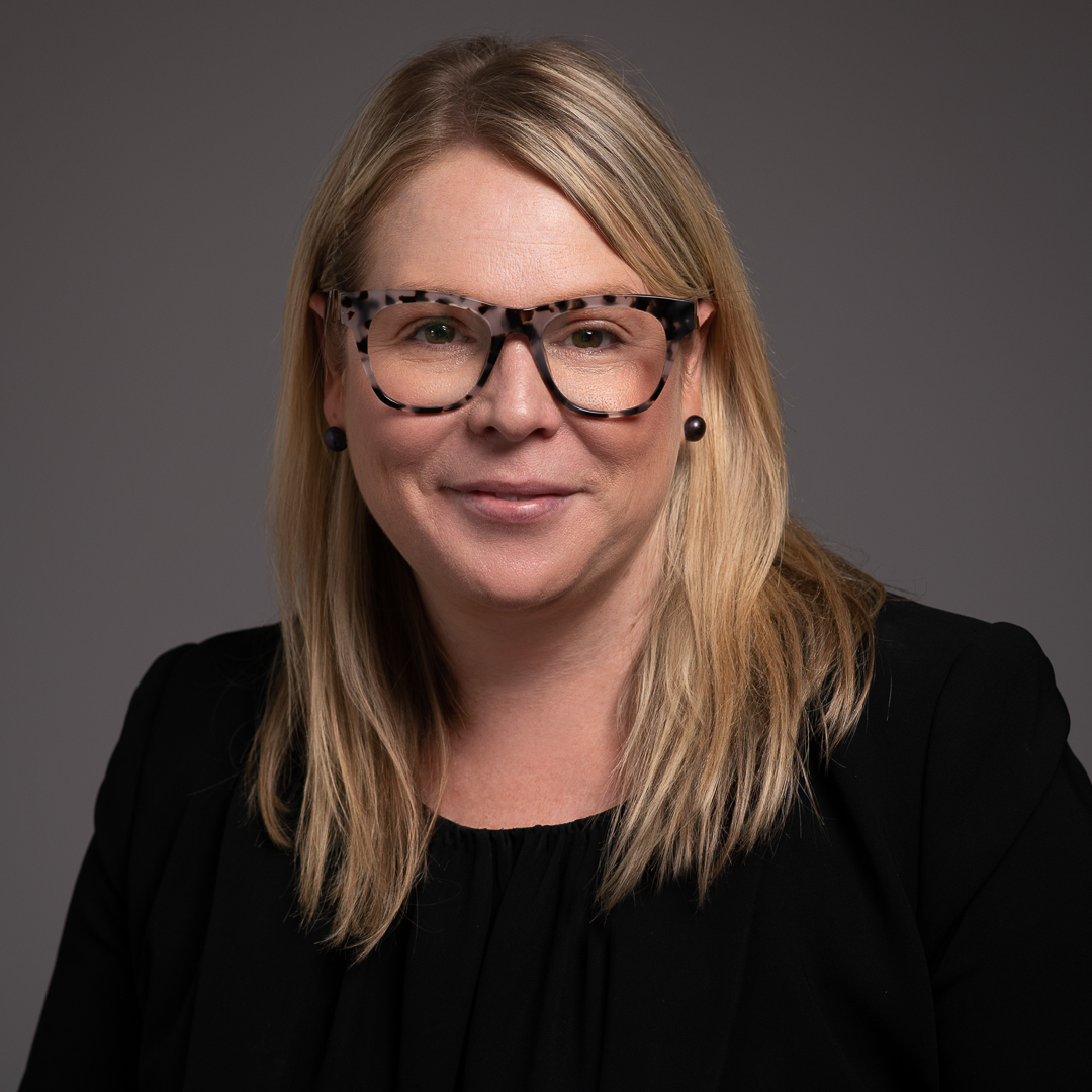 A linkedin headshot of melbourne barrister wearing glasses and a black top. She smiles to camera.