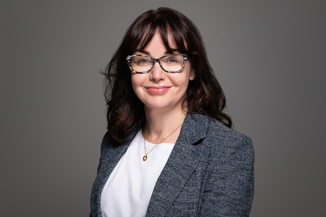 Melbourne woman smiles confidently to camera, wearing a grey blazer and patterned glasses for a relaxed but professional linkedin headshot.