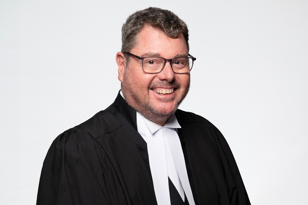 Melbourne barrister headshot of man wearing formal robes, smiling to camera confidently.