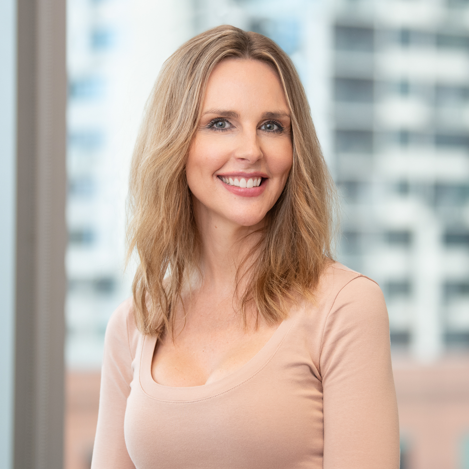 Melbourne Lawyer headshot with a city skyline building in the background. Woman is smiling at the camera.