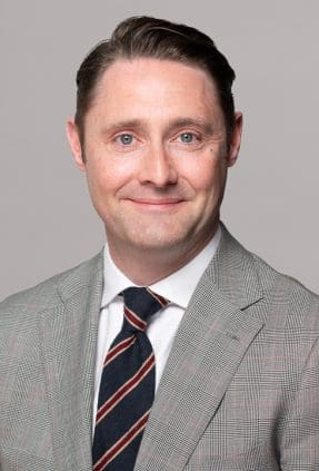 Melbourne LinkedIn headshot for local barrister, wearing a light grey checked suit, smiling to camera.