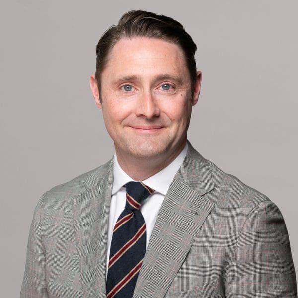 Melbourne LinkedIn headshot for local barrister, wearing a light grey checked suit, smiling to camera.