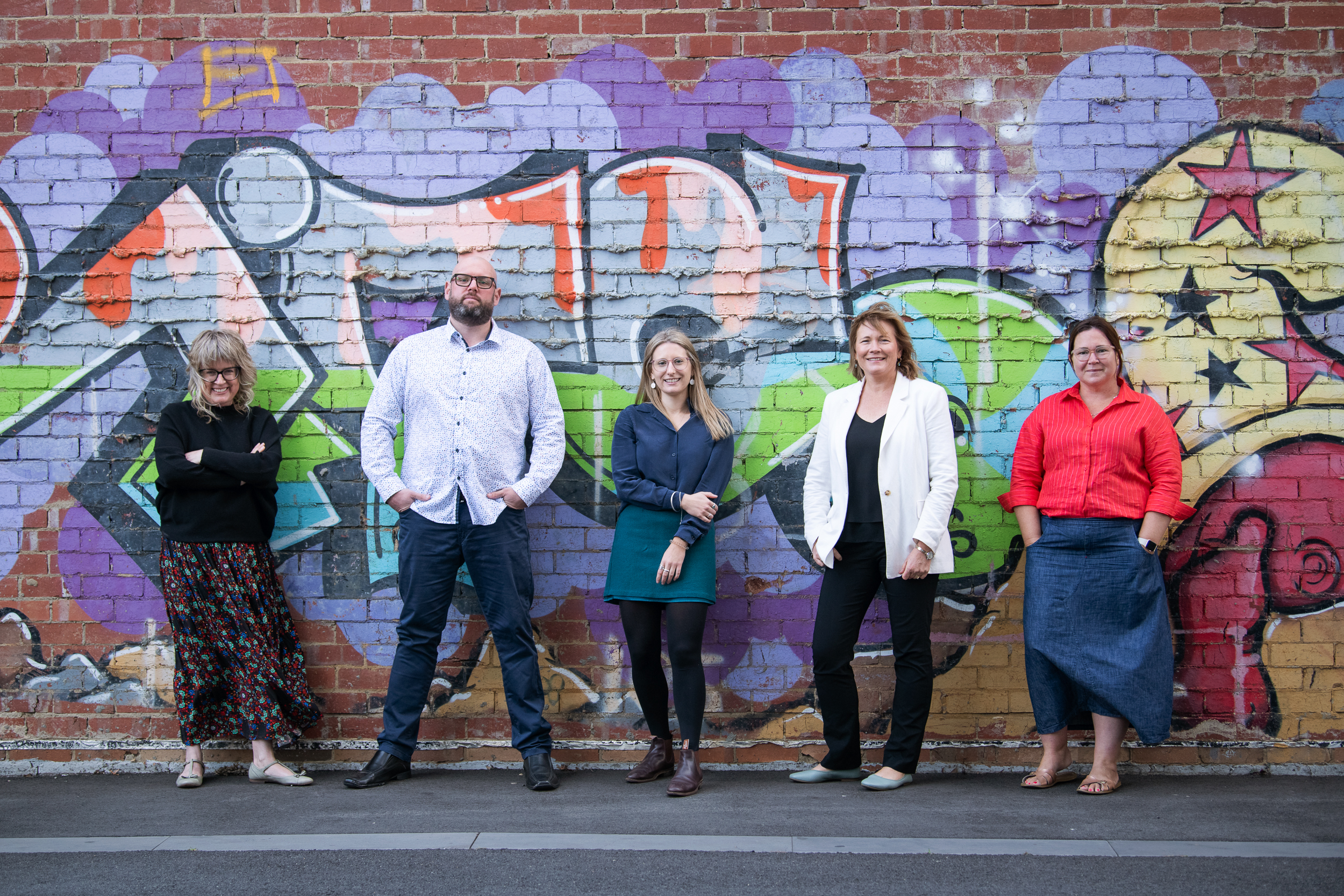 Melbourne team and staff photography. Personal branding group portraits of team collaborating and working together. This image shows a group portrait of 5 people standing in front of a graffiti wall.