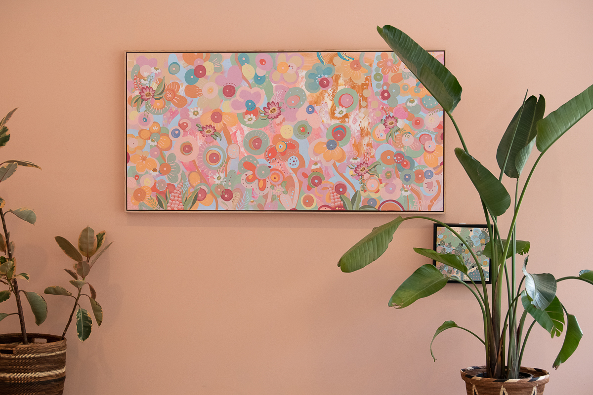 Detail image of artwork featured in Aurora Art Gallery. Image shows a panoramic framed canvas filled with colour (prominently pinks, reds and oranges) as well as indoor plants.