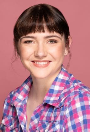 Studio actor headshot of young Melbourne woman smiling to camera wearing pink checks on a pink background.
